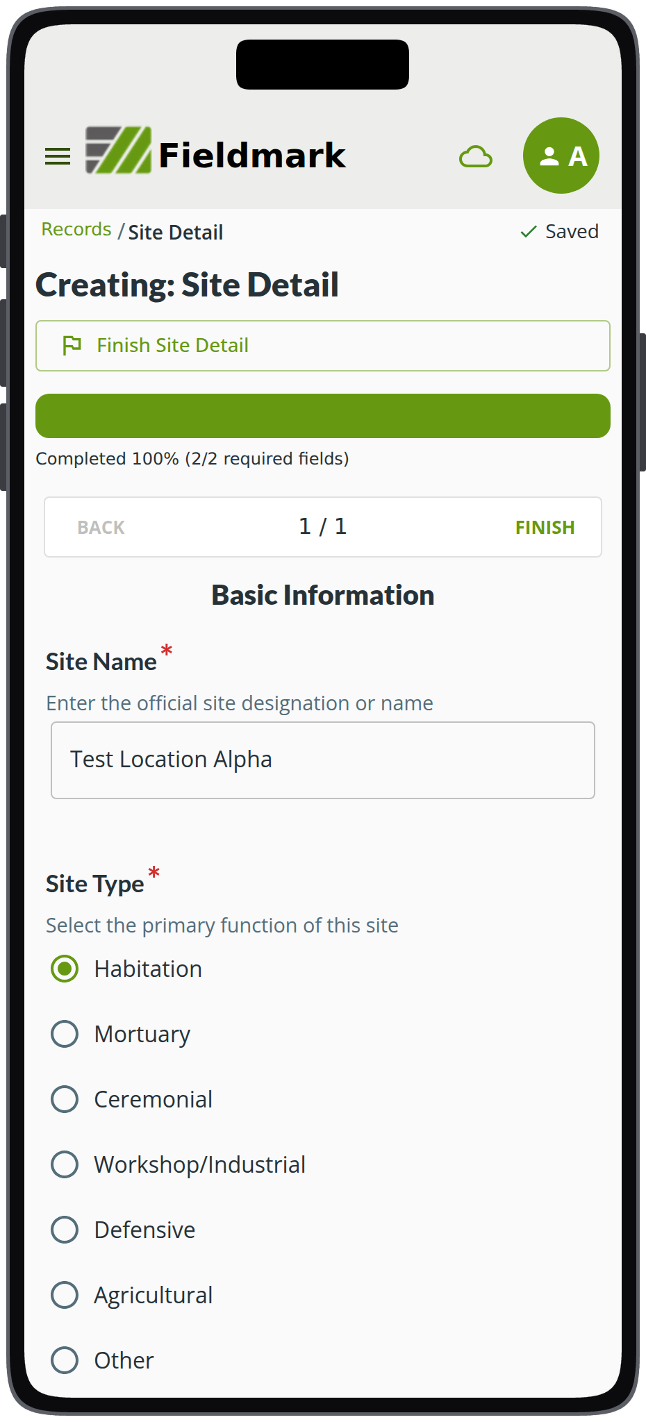 The Fieldmark app on a phone, with a record open on a form called Site Detail. The heading reads Creating: Site Detail, above a Finish Site Detail control, a full progress bar marked Completed 100% (2/2 required fields), and a row reading BACK, 1 / 1, FINISH. The section Basic Information follows: Site Name, marked required, holding Test Location Alpha, then Site Type, marked required, a list of radio buttons with Habitation selected above Mortuary, Ceremonial, Workshop/Industrial, Defensive, Agricultural, and Other.